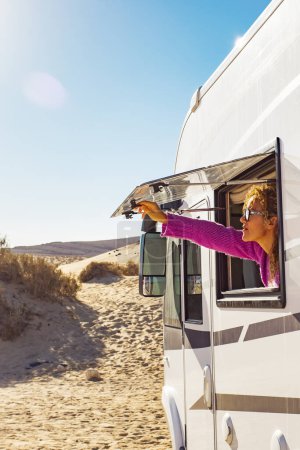 Photo for Adult tourist woman opening camper van window to enjoy the sun and freedom. Concept of travel people for summer holiday vacation inside camping car motorhome vehicle. Freedom nomad lifestyle - Royalty Free Image