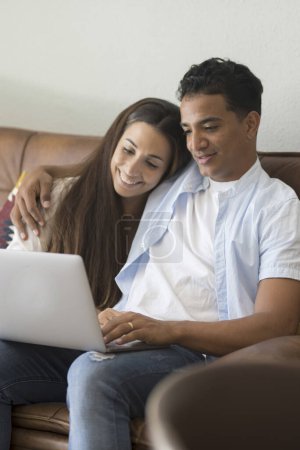 Téléchargez les photos : Jeune couple déménageant dans une nouvelle maison détente assis sur le canapé à l'aide d'un ordinateur portable, souriant heureux de déménager dans un nouvel appartement - en image libre de droit