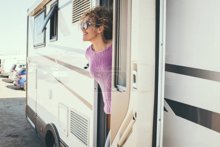 Téléchargez les photos : Femme regardant et souriant devant la porte d'un camping-car - en image libre de droit
