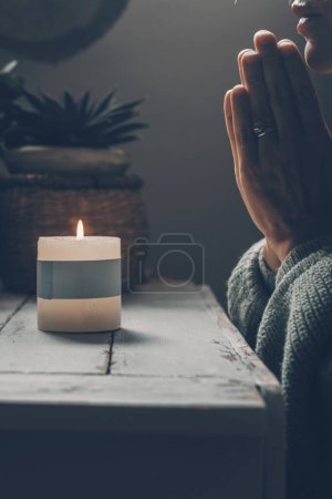 Foto de Mujer cristiana arrodillada y rezando cerca de la vela. Ella busca guía en su fe religiosa y espiritualidad. Espíritu del cristianismo y fe en la bondad de Dios - Imagen libre de derechos