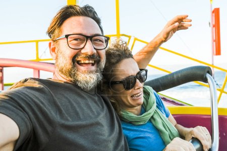 Photo for Adult couple have fun together on a roller coaster in an amusement park taking selfie picture with the phone. People enjoying holiday lifestyle. Mature man and woman enjoy time outdoor leisure activity - Royalty Free Image