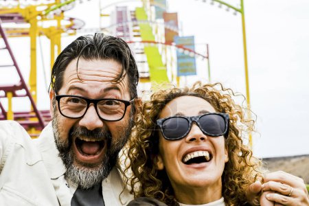 Photo for An adult couple of man and woman show expressions and fun during an extreme roller coaster ride. Smiling people have fun at playground during holidays and holidays,Outdoor recreation concept - Royalty Free Image