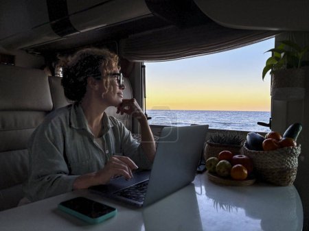 Photo for Modern adult woman digital nomad working on laptop sitting inside a motorhome camper van and using laptop computer with roaming traveler connection with phone on the table, Alternative job people - Royalty Free Image