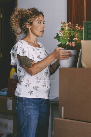 Téléchargez les photos : Woman preparing to move in a new house. Adult female enjoy unpacking her stuffs at home. Mortgage and apartment renting concept. People moving and loan. Caucasian middle age lady working indoor - en image libre de droit