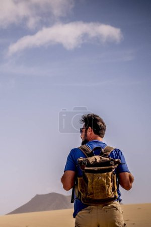 Photo for Adventure lifestyle with explorer man with backpack viewed from back walking in the desert and mountains alone - wild people alternative travel vacation alone in outdoor wild nature - Royalty Free Image