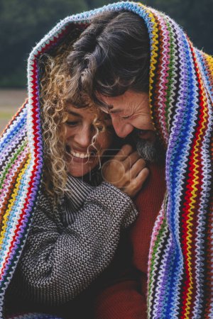 Téléchargez les photos : Moments intimes amusants et heureux avec un couple adulte dans une activité de loisirs de plein air couverte d'une couverture colorée tricotée au parc. couple homme et femme dans l'amour et la relation au parc ensemble - en image libre de droit