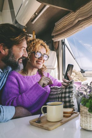 Photo for Tourist  adult people enjoy phone connection and freedom sitting inside a modern camper van and enjoying the beach outside. Concept of summer holiday couple travel vacation planning next destination - Royalty Free Image