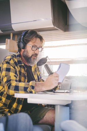 Photo for Modern adult man working with laptop and microphone inside a camper van in digital nomad job lifestyle. Technology and travel. Alternative freedom office concept with new activity and free people - Royalty Free Image