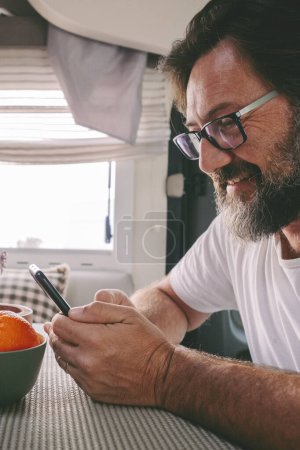 Photo for Side portrait of mature handsome man using phone sitting on a camper van. People and travel lifestyle with everywhere connection. People communicate during travel road trip. Planning destination - Royalty Free Image
