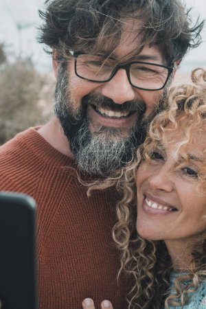 Photo for Happy adult  couple in love taking selfie picture outdoor. Cheerful man and woman doing video call. Pretty mature people enjoy love and relationship in leisure activity. Curly hair and beard - Royalty Free Image