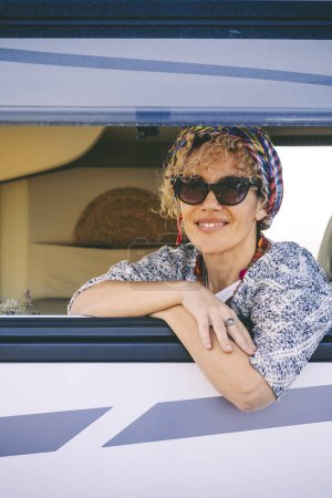 Photo for Portrait of woman smiling at the camper van window. Happy tourist enjoy travel vanlife lifestyle. Renting rv caravan for vacation leisure. Caucasian female cheers and enjoy holiday destination - Royalty Free Image