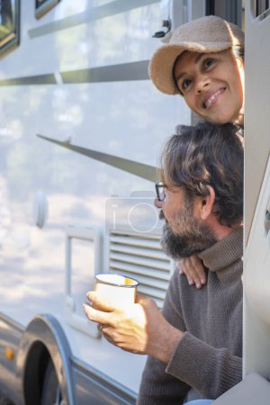 Photo for Couple of tourists with camper motor home sitting at the door enjoying nature outdoors leisure feeling. Travel people and mountains destination concept. Man and woman living van life together - Royalty Free Image