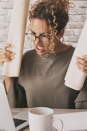 Téléchargez les photos : Femme en colère devant un ordinateur avec une expression mauvaise et stressée. Femme fatiguée travaillant sur ordinateur portable dans le lieu de travail de bureau à domicile. Concept de problèmes d'emploi et de technologie. Les gens dans une vie professionnelle intelligente - en image libre de droit