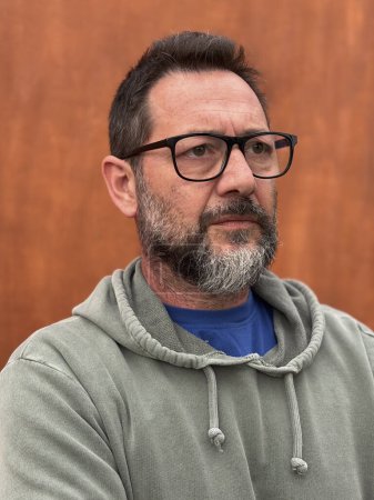 Photo for Portrait of pensive and worried adult man with beard and glasses. Crossed arms posture and severe unhappy eyesight. Mature male people with thougts. Brown background. - Royalty Free Image