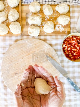 Téléchargez les photos : Vue de dessus de la femme préparant le déjeuner fait main comme le pain ou la pizza dans le travail traditionnel à la maison sur la table dans la cuisine. Personne méconnaissable préparer boulangerie fraîche avec les mains. Matières premières fraîches travailler - en image libre de droit