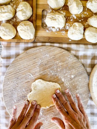 Téléchargez les photos : Vue de dessus de la femme préparant le déjeuner fait main comme le pain ou la pizza dans le travail traditionnel à la maison sur la table dans la cuisine. Personne méconnaissable préparer boulangerie fraîche avec les mains. Matières premières fraîches travailler - en image libre de droit