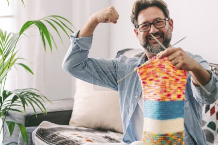Photo for Mature man proud show his knit work results sitting at home on the sofa alone with big smile and happy expression. Indoor leisure activity people. Good time lifestyle in apartment modern - Royalty Free Image