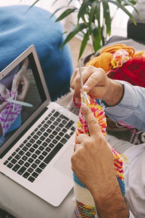 Photo for Man follow online lesson tutorial to learn new things like knitting work alone at home sitting comfortably on the sofa and enjoying time. Hobby and indoor leisure activity people relaxation - Royalty Free Image