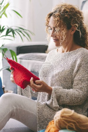 Foto de Mujer sentada en el suelo tejiendo una bola de lana roja. Creación hecha a mano relajante en una tarde de domingo. Concepto de estilo de vida y ocio - Imagen libre de derechos