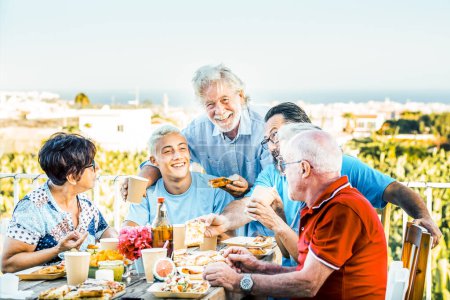 Foto de Familia multigeneracional almorzando en una terraza en un hermoso día soleado. Niño de 18 años se ríe con sus abuelos celebrando. Estilo de vida y concepto familiar - Imagen libre de derechos