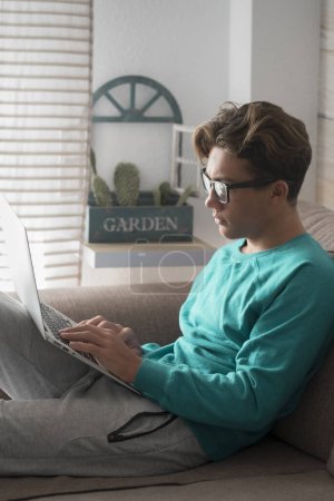 Téléchargez les photos : Jeune adolescent étudiant masculin à la maison faisant des cours en ligne leçons avec ordinateur portable technologie connectée à Internet - école et concept d'étude dans le temps de verrouillage du coronavirus covid-19 - en image libre de droit