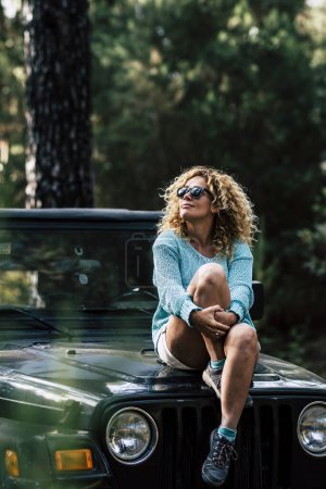 Foto de Hermosa mujer sentarse en el coche todoterreno y disfrutar de la naturaleza alrededor - concepto de vacaciones fuera de la red y viaje con madera y árboles - la gente disfruta de la actividad de ocio al aire libre con vehículo - Imagen libre de derechos