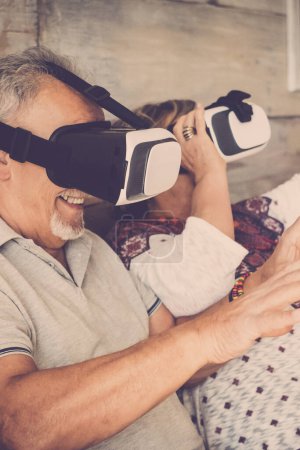 Téléchargez les photos : Couple de personnes âgées profitant à la maison de la nouvelle technologie casque goggled avec des lunettes et la réalité virtuelle rester à la maison et s'amuser ensemble retraité homme et femme - en image libre de droit