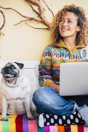 Foto de Mujer feliz pareja y perro divertido en casa sentado en una cubierta de color divertirse y utilizar la tecnología ordenador portátil - bloqueo y oficina en casa inteligente trabajo estilo de vida - Imagen libre de derechos