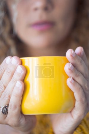 Téléchargez les photos : Gros plan de tasse jaune de thé ou de café femme caucasienne tenant boisson chaude à la maison à l'intérieur - concept de quarantaine covid-19 coronavirus rester à la maison - en image libre de droit