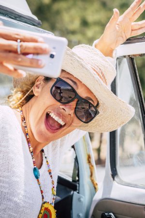 Photo for Happy and cheerful young beautiful caucasian lady take selfie picture outside her retro van vehicle enjoying the trip and travel lifestyle - summer holiday vacation lifestyle - Royalty Free Image