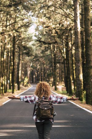 Téléchargez les photos : Concept de réussite et de liberté avec femme et sac à dos vus de dos et longue route asphaltée directement au milieu d'une forêt naturelle de hauts arbres la vie après verrouillage du coronavirus - en image libre de droit