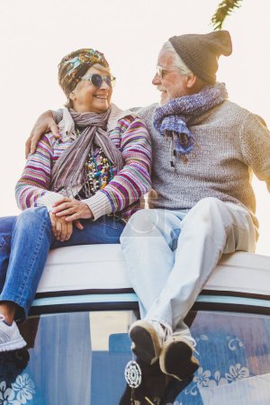 Foto de Un par de viejos viajeros mayores se sientan juntos en el techo de la furgoneta disfrutan de la puesta del sol junto con el amor - para siempre y el concepto de vacaciones para los viajeros jubilados - Imagen libre de derechos