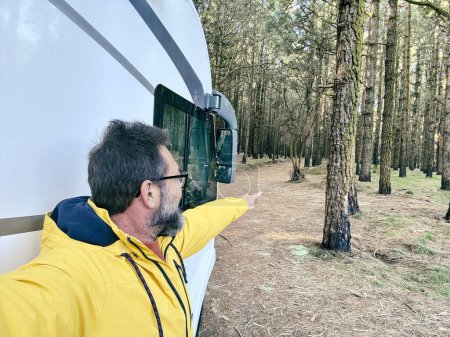 Photo for Adult man taking selfie picture outside a camper van motorhome parking in the nature park outdoors with trees. People and travel alternative lifestyle vanlife vacation renting vehicle. Leisure - Royalty Free Image