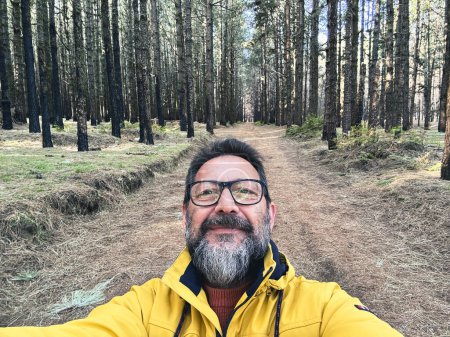 Téléchargez les photos : Joyeux homme heureux adulte prenant des photos selfie dans les bois profitant d'activités de loisirs en plein air dans le parc forestier national seul. Aventure et mode de vie. Hauts arbres en arrière-plan. Durabilité - en image libre de droit