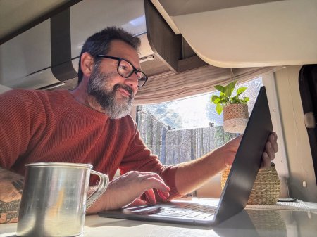 Téléchargez les photos : Nomade numérique travaillant à l'intérieur d'un camping-car Voyage style de vie véhicule vanlife à l'aide d'un ordinateur portable et une connexion Internet en itinérance. Les gens et le télétravail à distance. La vie en camping-car. Moderne - en image libre de droit