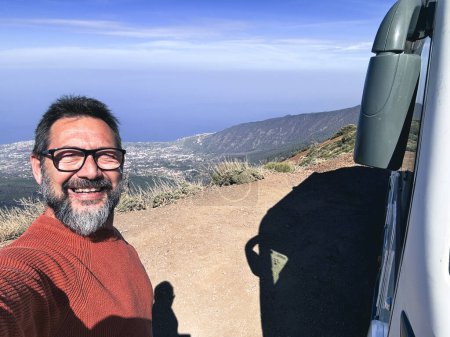 Photo for Adult man taking selfie picture outside a camper van motorhome parking in the mountain scenic view background. People and travel alternative lifestyle vanlife vacation renting vehicle. - Royalty Free Image