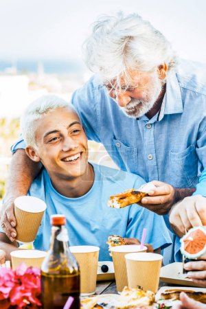 Photo for Multigenerational family having lunch on a terrace on a beautiful sunny day. 18-year-old boy laughs with his grandparent celebrating. Lifestyle and family concept - Royalty Free Image