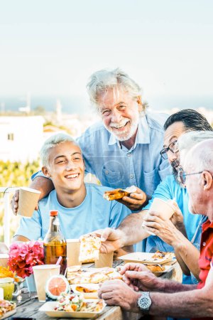 Photo for Multigenerational family having lunch on a terrace on a beautiful sunny day. 18 year old boy laughs with his grandparents celebrating. Lifestyle and family concept - Royalty Free Image