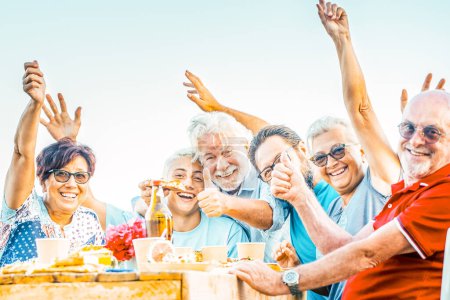 Foto de Generaciones familiares disfrutan y celebran con diversión todos juntos riendo y sonriendo posando para una foto al aire libre en casa - mesa llena de comida y bebidas para comer para las personas caucásicas - Imagen libre de derechos