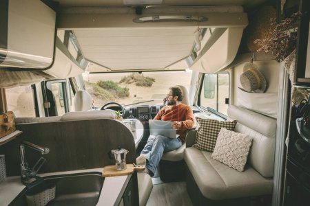 Photo for Handsome man with glasses sitting inside camper van, looking into the distance and smiling. Camping, outdoor activity, road trip, nature concept. - Royalty Free Image