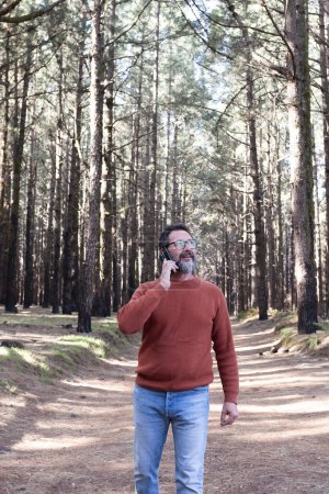 Photo for Man using phone  in a forest wood enjoying technology and outdoor leisure activity. Modern man speaking at cellular with trees in background. People and communication on travel - Royalty Free Image