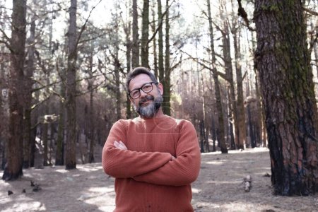 Photo for Portrait of adult man with crossed arms in a forest woods with trees and sunlight in background. Concept of people and nature. Outdoor leisure activity. Activist against deforestation. - Royalty Free Image