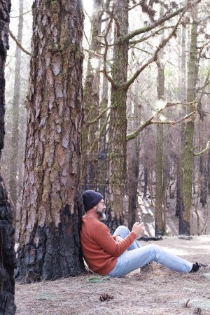 Téléchargez les photos : Un homme utilisant le téléphone dans un bois forestier profitant de la technologie et des loisirs de plein air. Homme moderne parlant au cellulaire avec des arbres en arrière-plan. Personnes et communication sur les voyages - en image libre de droit