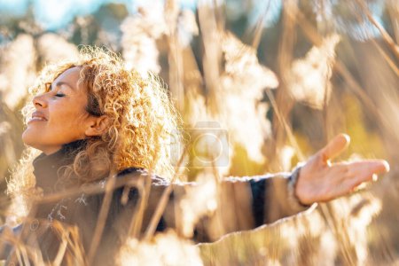 Foto de Mujer feliz extendiendo los brazos en un campo de hierba de color amarillo alto en la puesta del sol luz del sol de oro sonriendo y respirando para disfrutar de la naturaleza y el amor medio ambiente y sostenibilidad. Personas éxito femenino estilo de vida - Imagen libre de derechos