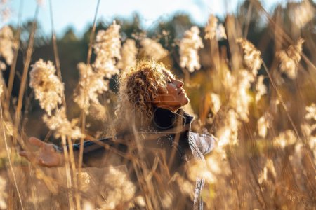 Téléchargez les photos : Femme heureuse étendant les bras dans un champ de hautes herbes jaunes au coucher du soleil doré soleil souriant et respirant pour profiter de la nature et l'environnement amour et la durabilité. Personnes style de vie succès féminin - en image libre de droit