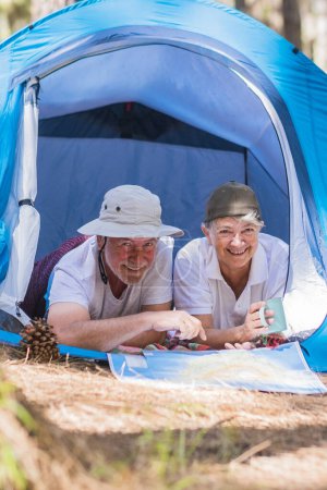 Photo for Couple of active traveler senior people enjoy together inside a tent in free camping in the forest - young retired people and free alternative lifestyle concept with love for nature - travel life at every age - Royalty Free Image