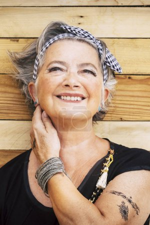 Téléchargez les photos : Portrait de femme heureuse âgée caucasienne joyeuse avec un fond en bois - sourire alternatif et jeune vieille femme et profiter - peau tatouée pour le concept de diversité et l'âge - mode de vie jeune - en image libre de droit