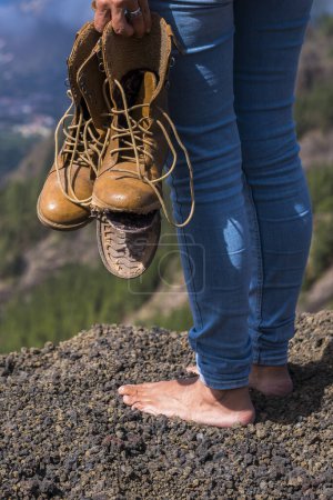 Téléchargez les photos : Voyage et wanderlust concept de style de vie avec femme pieds nus se lever avec des chaussures cassées sur les mains en regardant la vue sur le sommet de la montagne - en image libre de droit
