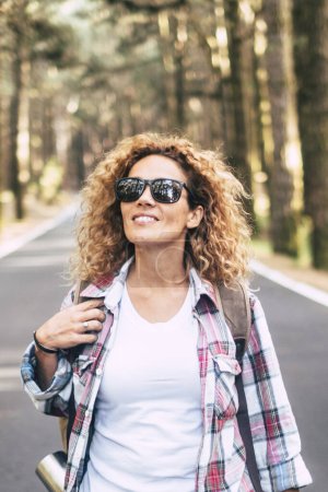 Photo for Happy travel wanderlust lifestyle with cheerful  caucasian woman walking and traveling on a road with forest and beautiful nature wood around - Royalty Free Image