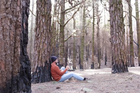 Téléchargez les photos : Un homme utilisant le téléphone dans un bois forestier profitant de la technologie et des loisirs de plein air. Homme moderne parlant au cellulaire avec des arbres en arrière-plan. Personnes et communication sur les voyages - en image libre de droit